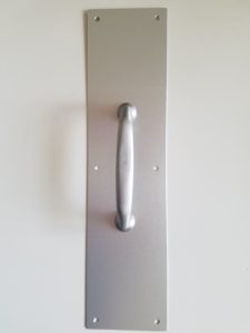 Pull handle with backplate used on commercial entry doors with manual access setups.