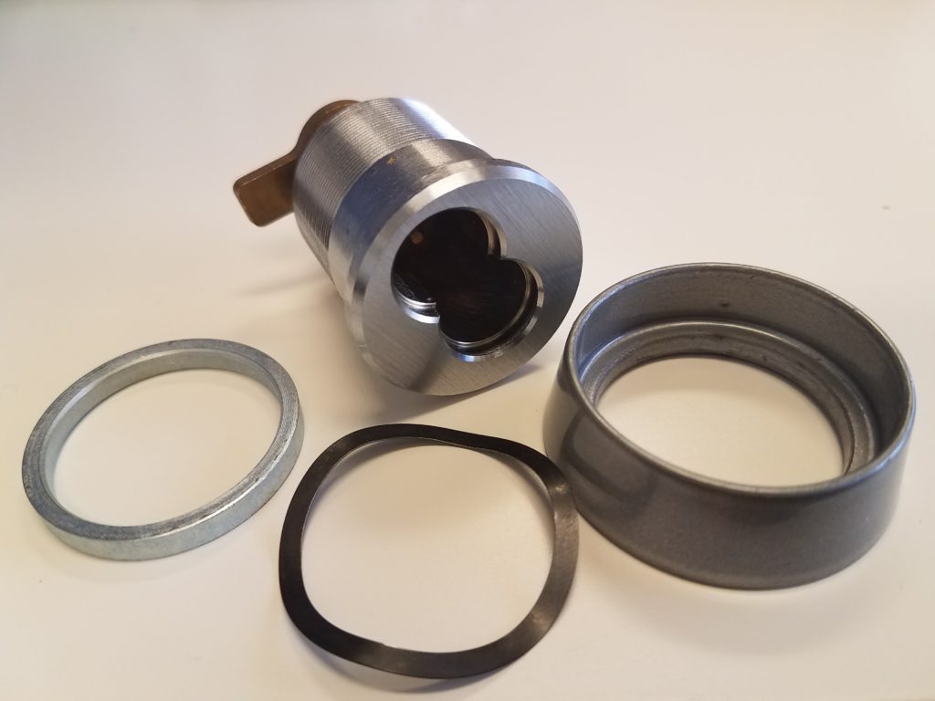 Disassembled mortise cylinder housing and components used for commercial door lock installations.