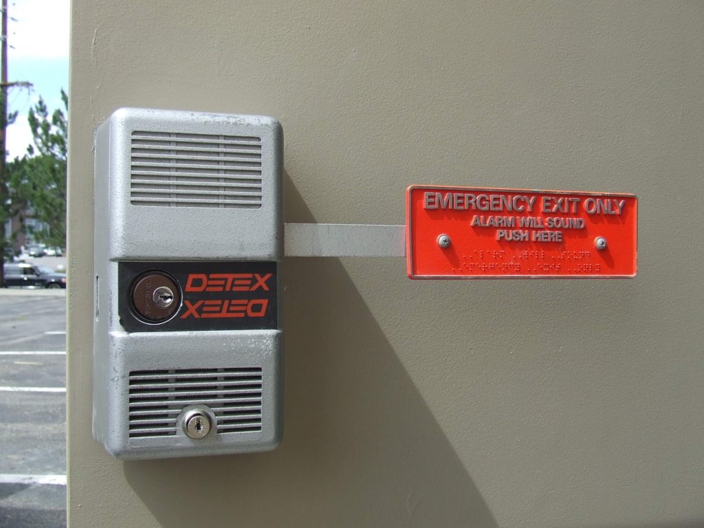Detex emergency exit alarm lock with keyed cylinder, commonly rekeyed in commercial properties for security.