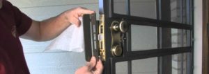 Technician servicing a metal security door lock and deadbolt on a residential property.