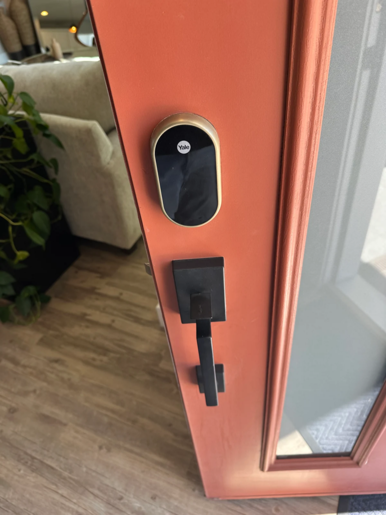 Yale electronic door lock above a black handle on a coral-colored door with glass.