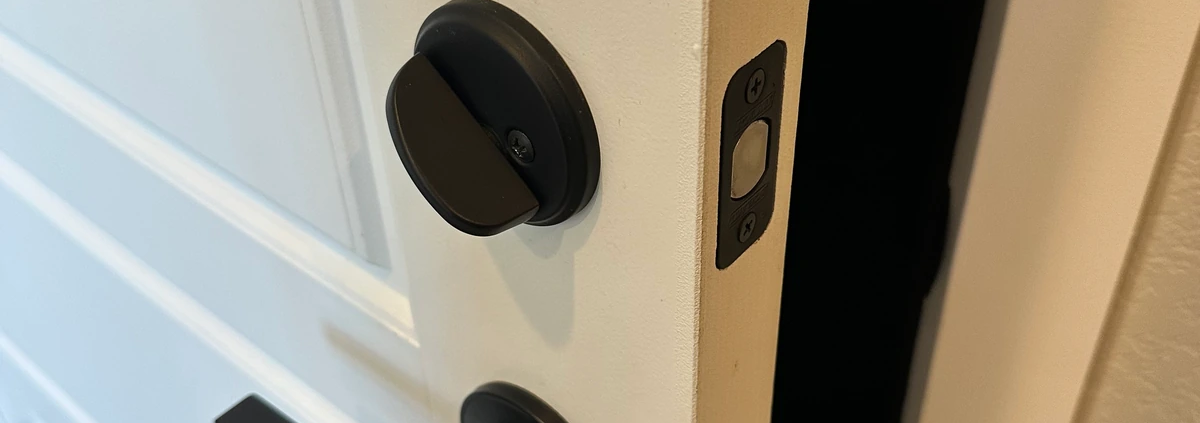 Black deadbolt and lever handle on an open white door.